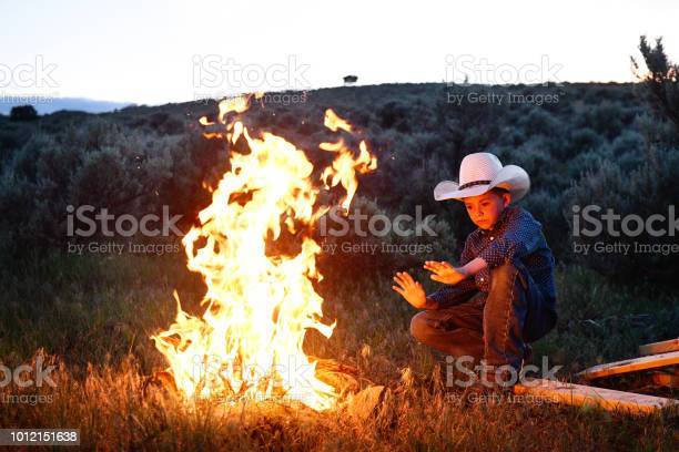 ern-american-boy-in-cowboy-hat-stays-warm-by-fire-at-dusk-in-utah-picture-id1012151638?s=612x612.jpg